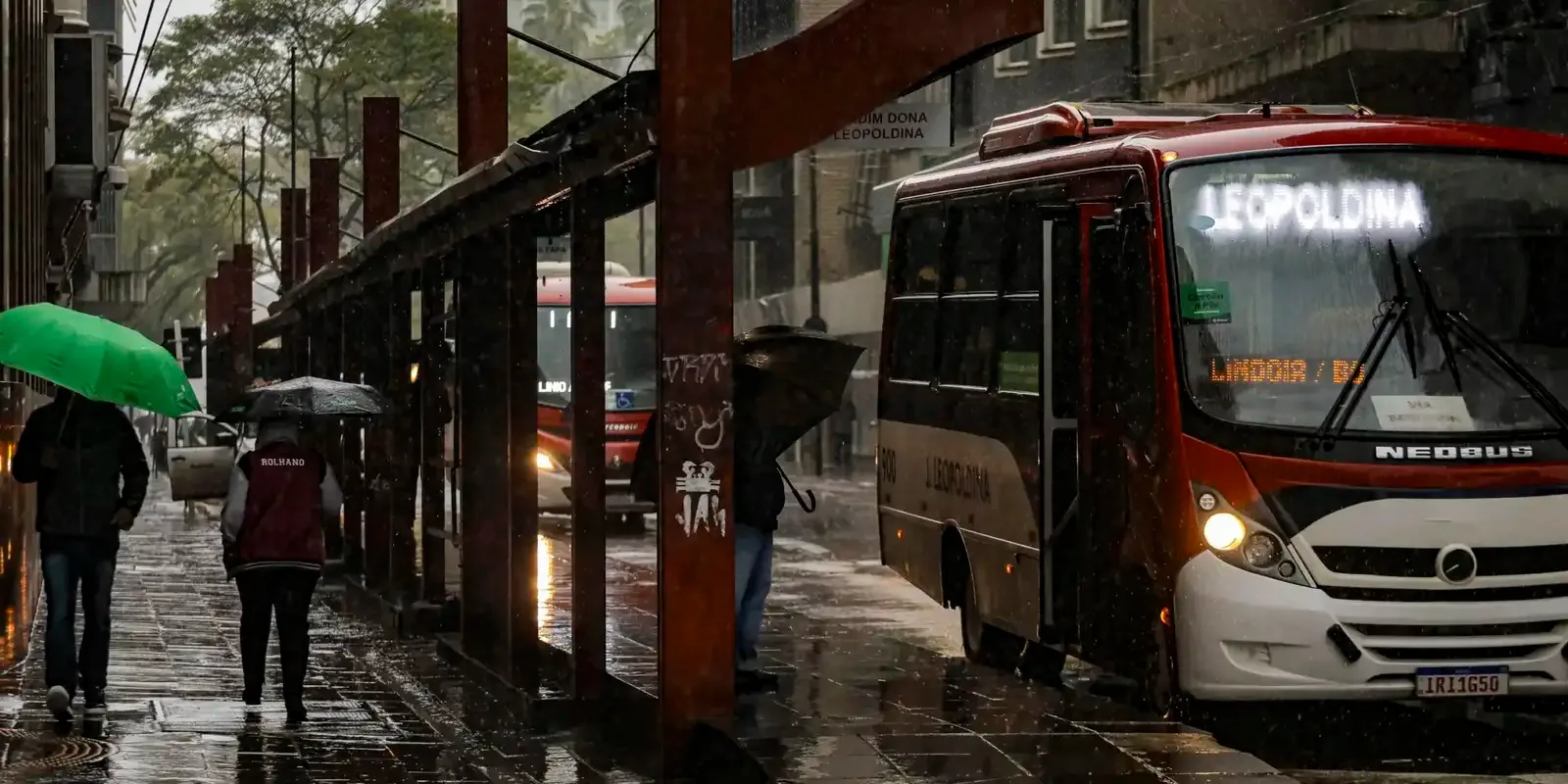 Chuva forte sobre rua de cidade brasileira com pedestres usando guarda-chuva