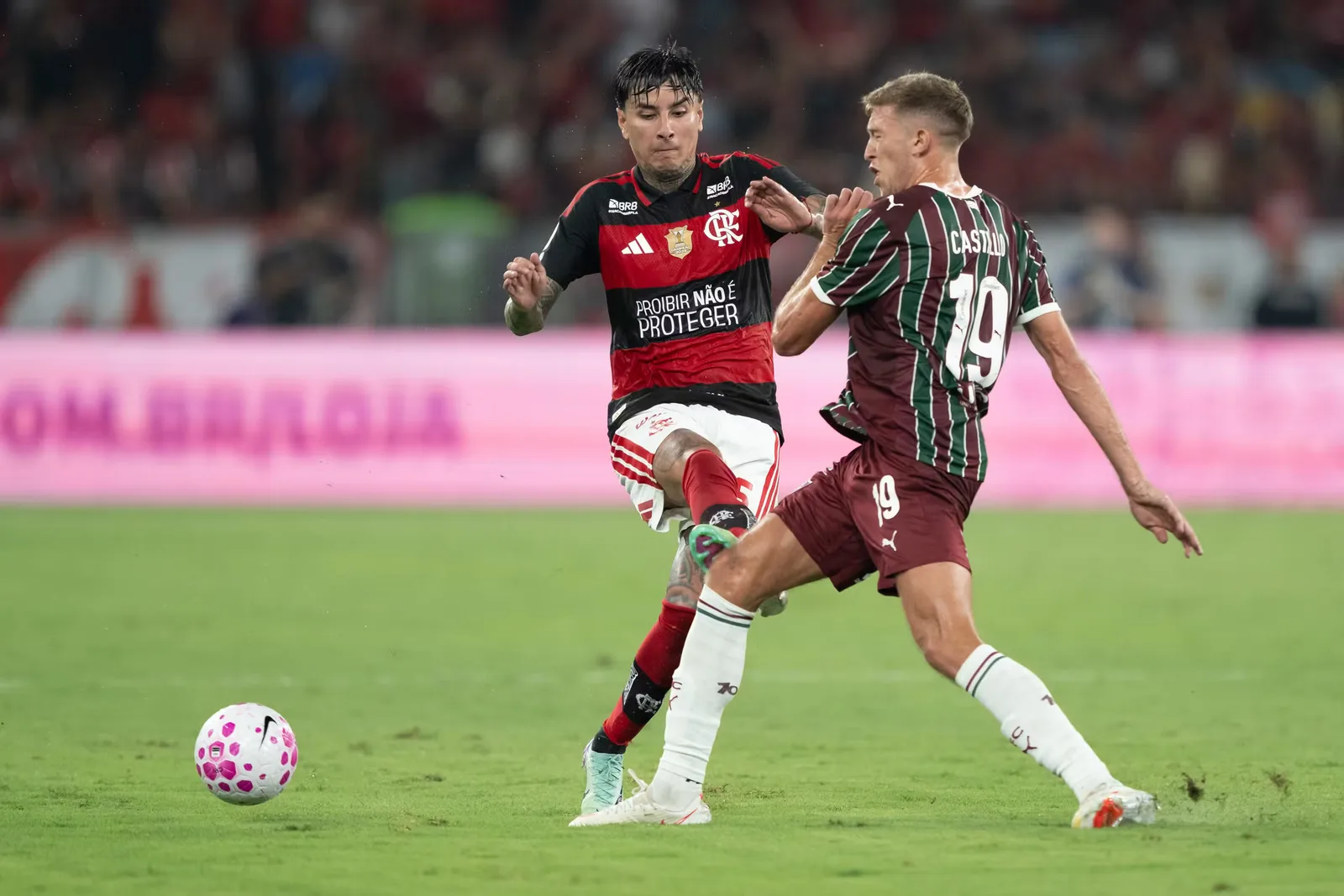 Jogador de uniforme vermelho em disputa de bola durante partida no Maracanã