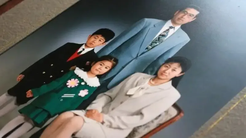Em um retrato formal de família, quatro pessoas posam diante de um fundo escuro de estúdio. Em primeiro plano, uma mulher está sentada em uma cadeira e usa um